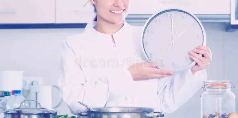 Girl in chef uniform with clock and veggies at kitchen stock photo